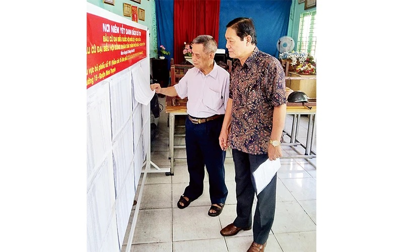Ông Nguyễn Tài On (người bên phải) hướng dẫn người dân xem danh sách cử tri.