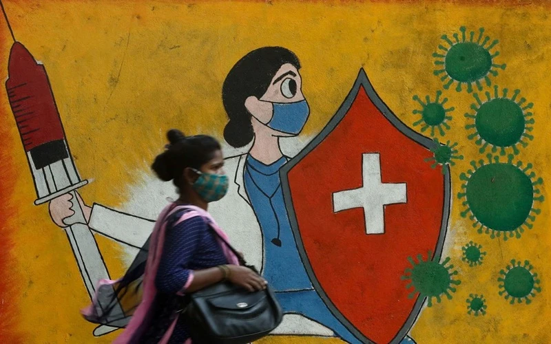 Người phụ nữ đi qua bức tường có tranh cổ động người dân tiêm phòng Covid-19 tại Mumbai, Ấn Độ. (Ảnh: Reuters)