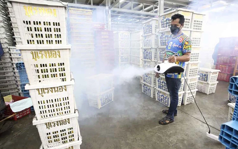 Một người bán hoa quả đang  phun thuốc khử khuẩn vào gian hàng của mình nhằm giảm nguy cơ nhiễm Covid-19. (Ảnh: Bangkok Post)