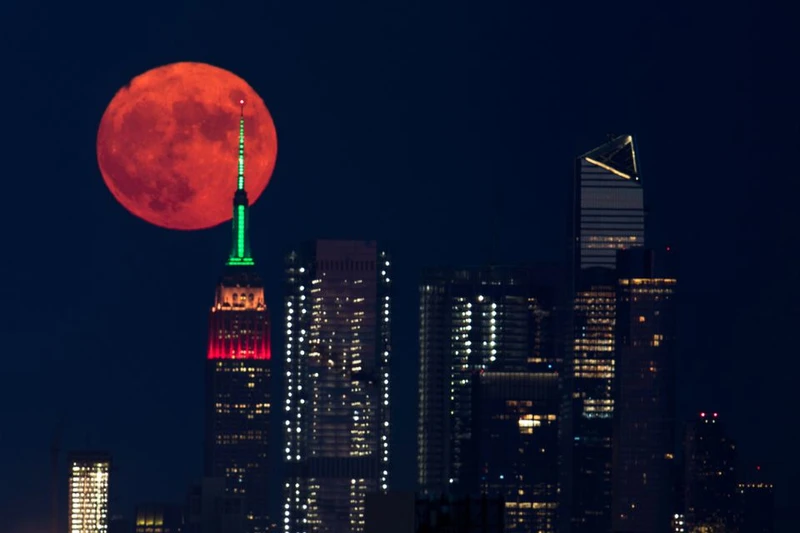 Trăng tròn màu cam đỏ mọc sau Tòa nhà Empire State ở thành phố New York, Mỹ tối 23/7. Ảnh: Reuters.