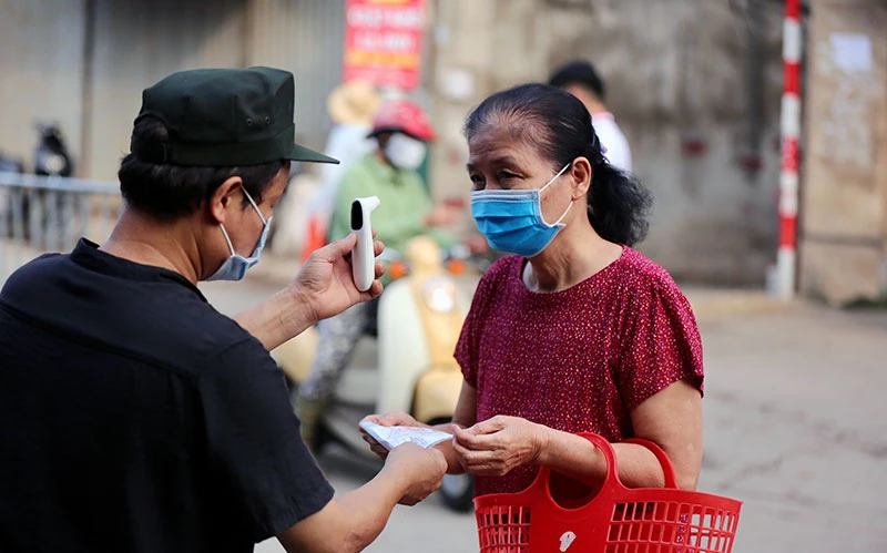Lực lượng chức năng phường Nhật Tân (quận Tây Hồ) kiểm tra thân nhiệt và thẻ đi chợ của người dân. Ảnh: MINH SƠN 