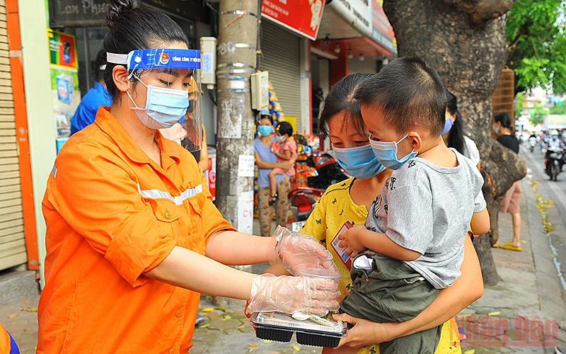 Tình nguyện viên của Đoàn thanh niên EVNNPC trao những suất cơm nghĩa tình tặng gia đình các bệnh nhi tại ngõ 947 Đê La Thành (TP Hà Nội). (Ảnh: LINH PHAN) 