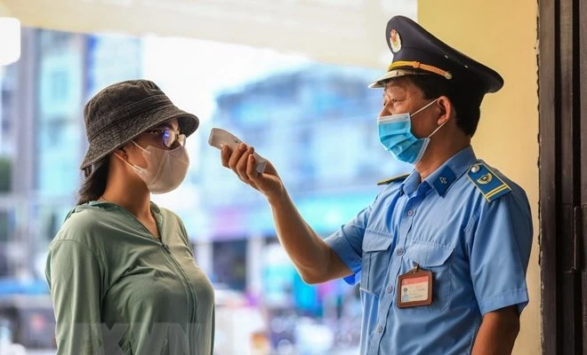 Nhân viên an ninh nhà ga Hà Nội kiểm tra thân nhiệt cho khách đến mua vé tàu sáng 12/10. (Ảnh: Thành Đạt/TTXVN)
