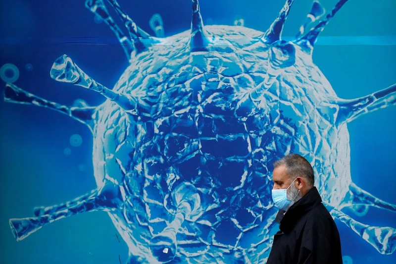 Một người đàn ông đeo khẩu trang đi ngang qua hình ảnh minh họa của virus corona ở Anh. Ảnh: Reuters.