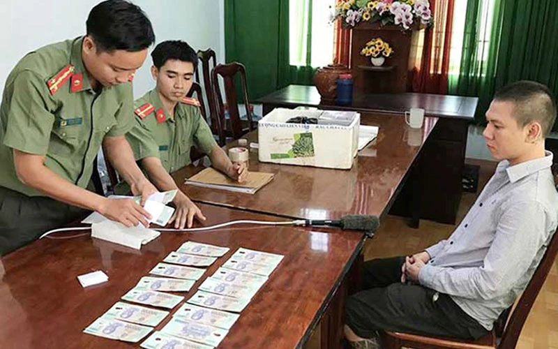Ðối tượng Nguyễn Ðức Huy (32 tuổi, ở phường 5, quận 10, thành phố Hồ Chí Minh) và số tiền giả bị thu giữ tại Cơ quan An ninh điều tra Công an tỉnh Ðắk Nông. Ảnh: ÁNH XUÂN 