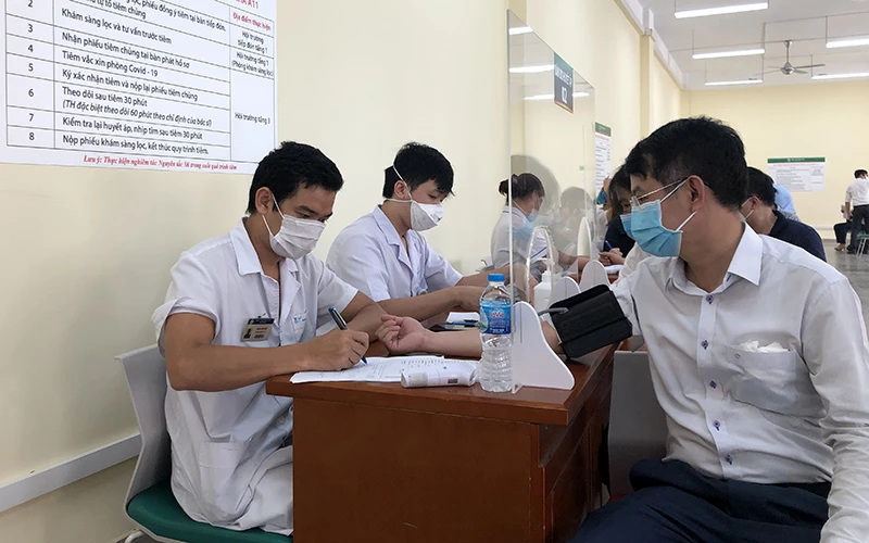 Nhân viên y tế Bệnh viện Bạch Mai (Hà Nội) khám cho người dân trước khi tiêm vắc-xin phòng Covid-19. Ảnh: HỮU NGUYÊN