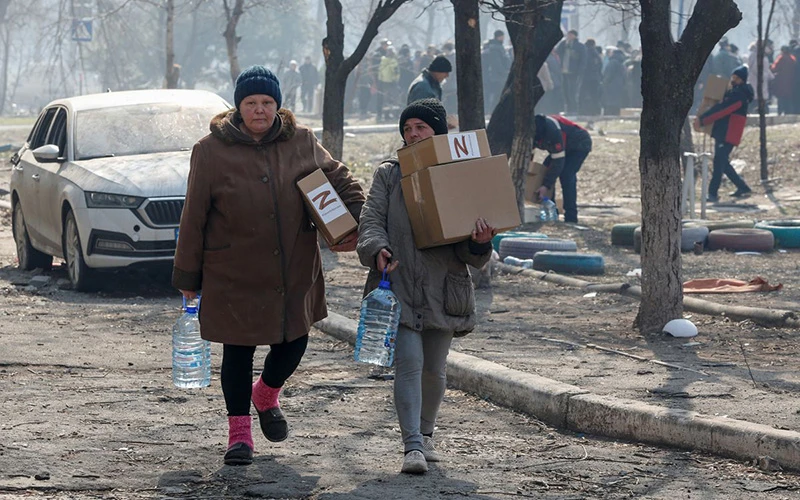 Người dân địa phương mang hàng viện trợ nhân đạo do binh sĩ Nga phân phát tại khu vực cảng Mariupol, Ukraine, ngày 23/3. (Ảnh: Reuters)
