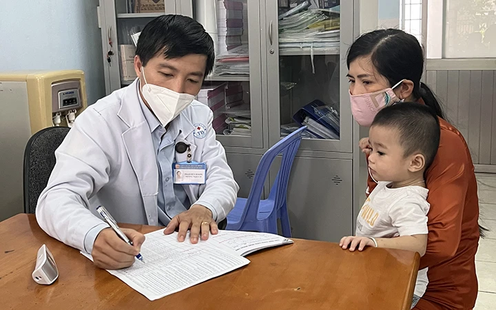 Bác sĩ Phạm Huy Hoàng, Trưởng trạm Y tế phường Trường Thọ, thành phố Thủ Đức, TP Hồ Chí Minh, khám bệnh cho trẻ. (Ảnh: Mạnh Hảo)