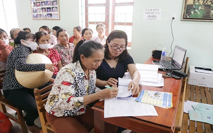 Bà Trần Thị Hiên (người cầm bút) nộp tiền tham gia bảo hiểm xã hội tự nguyện tại Hội nghị tuyên truyền. (Ảnh PHẠM CHÍNH)