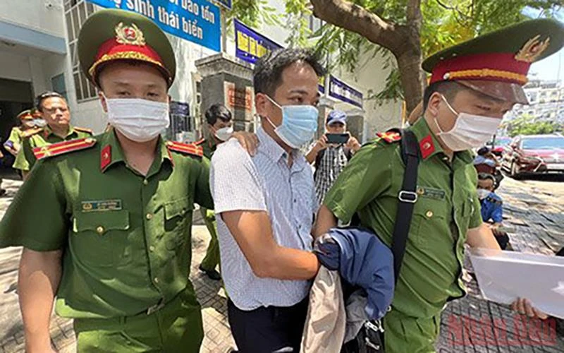 Cảnh sát áp giải ông Trần Quốc Huy, Trưởng Phòng Tổ chức-Hành chính CDC Khánh Hòa rời khỏi trụ sở làm việc. (Ảnh: THÀNH LONG)