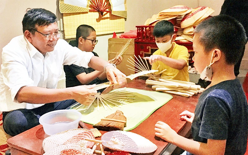 Nghệ nhân Dương Văn Ðoàn hướng dẫn các em nhỏ làm quạt. 