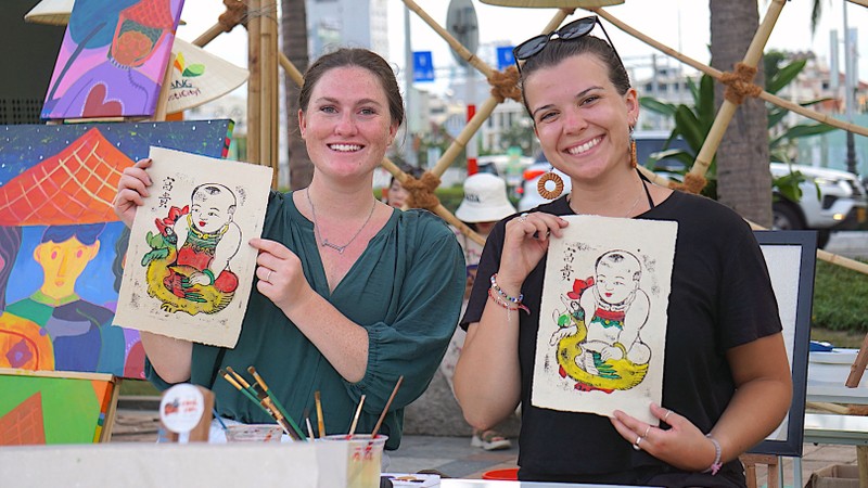 Các chị Kassidee và Izzy (du khách Mỹ) thích thú khi trải nghiệm làm tranh Ðông Hồ tại Lễ hội Tận hưởng mùa hè 2023-Enjoy Danang 2023. 