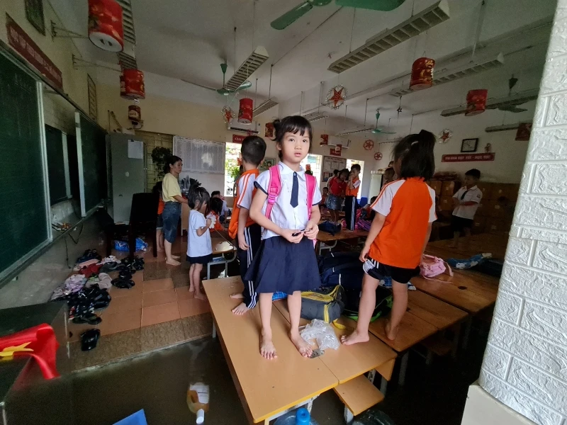 Nước tràn vào lớp tại trường Tiểu học Phú Lương 2 (quận Hà Đông) khiến cho học sinh phải đứng cả lên bàn để tránh. (Ảnh: CTV)