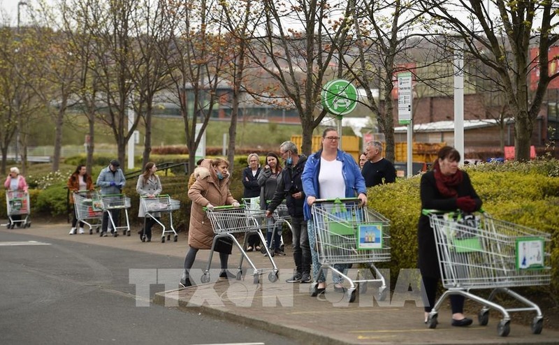 Người dân thực hiện giãn cách xã hội phòng lây nhiễm Covid-19 khi xếp hàng chờ mua sắm bên ngoài 1 siêu thị ở Gateshead, Anh, ngày 9/4/2020. (Ảnh: AFP/TTXVN)