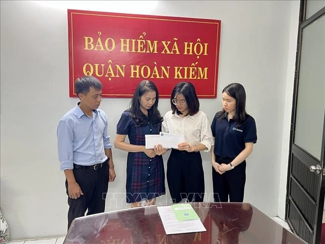 Đại diện lãnh đạo Bảo hiểm xã hội quận Hoàn Kiếm trao các chế độ tử tuất và mai táng phí cho gia đình người bị nạn. Ảnh: TTXVN phát