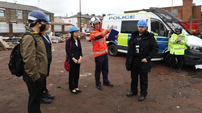 Tham tán, Phó Đại sứ Tô Minh Thu (thứ 3 từ trái sang) trao đổi với các lực lượng chức năng Manchester tại hiện trường vụ cháy. (Ảnh: Đình Thư/TTXVN)