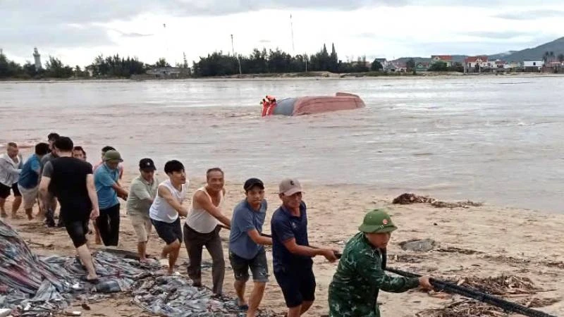 Bộ đội biên phòng và người dân hợp sức neo buộc tàu cá bị lật chờ nước lũ sông Gianh giảm để trục vớt.