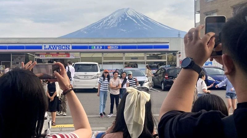 Khách du lịch chụp ảnh với khung cảnh núi Phú Sĩ phía sau cửa hàng tiện lợi Lawson ở thị trấn Fujikawaguchiko, tỉnh Yamanashi, Nhật Bản, ngày 28/4/2024. (Ảnh: Reuters/Kyodo) 