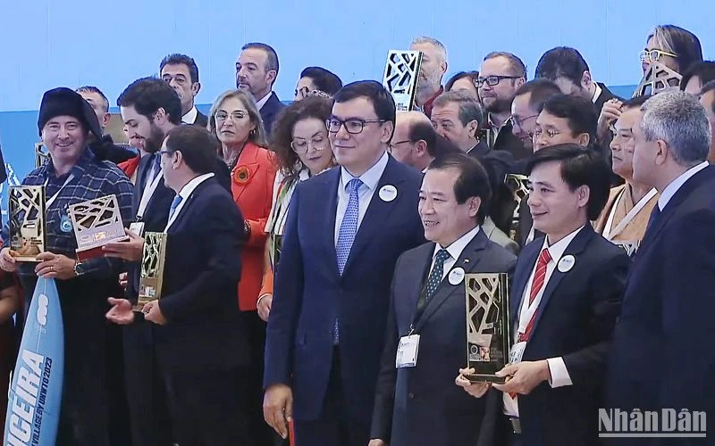 Chủ tịch UBND xã Tân Hóa nhận Giải thưởng “Làng du lịch tốt nhất” của UNWTO với sự chúc mừng của Phó Cục trưởng Hà Văn Siêu và Tổng Thư ký UNWTO Zurab Pololikashvili. (Ảnh chụp từ clip của UNWTO) 