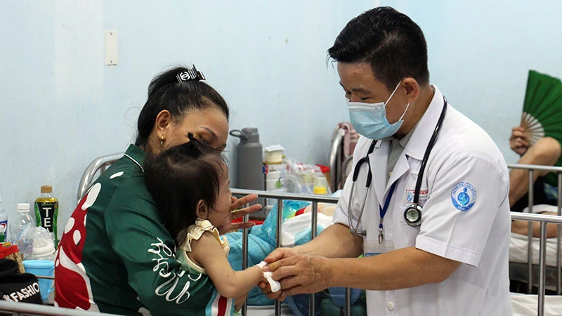 Bác sĩ Bệnh viện Nhi đồng 1 Thành phố Hồ Chí Minh thăm khám cho trẻ mắc tay chân miệng. (Ảnh THẾ ANH)