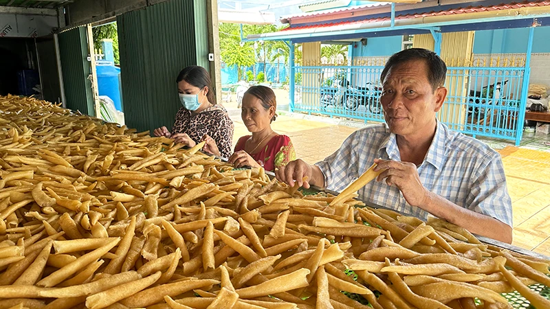 Thương binh Trần Văn Khi hướng dẫn lao động dân tộc Khmer cách chế biến đặc sản bong bóng cá biển. (Ảnh NGUYỄN PHONG)