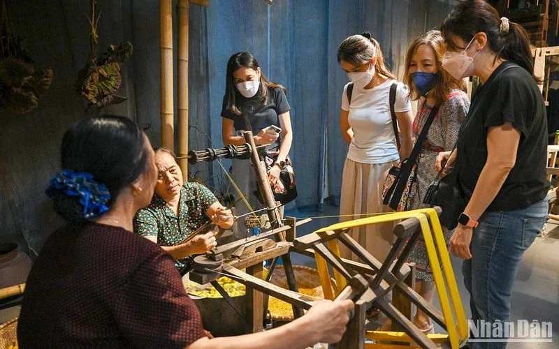 Du khách nước ngoài tìm hiểu về nghề ươm tơ, dệt vải truyền thống tại triển lãm “Muôn nẻo đường tơ”. (Ảnh DUY ĐĂNG)