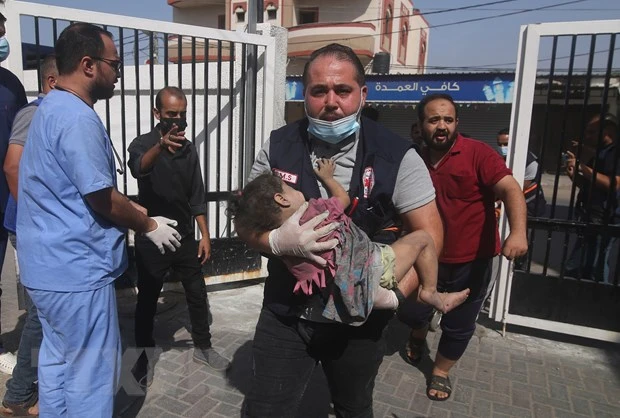 Người đàn ông ôm một em nhỏ bị thương sau cuộc không kích của Israel xuống Dải Gaza ngày 23/10/2023. (Ảnh: THX/TTXVN)