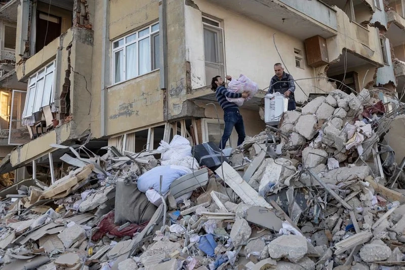 Hai cha con mang đồ đạc rời khỏi căn hộ bị sập tại tỉnh Hatay, Thổ Nhĩ Kỳ. (Ảnh: Reuters)