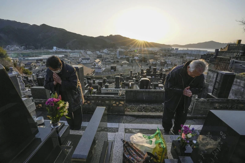 Người đàn ông cùng vợ cầu nguyện trước phần mộ của người thân tại Otsuchi, tỉnh Iwate. (Ảnh: Kyodo)
