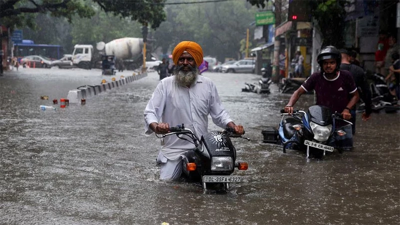 Người dân cùng phương tiện giao thông vượt qua tuyến đường bị ngập tại New Delhi, ngày 8/7/2023. (Ảnh: Reuters)