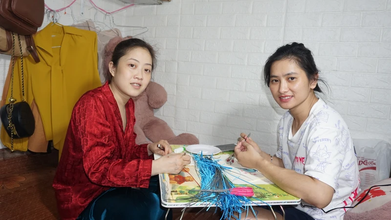 Chị Trang (bên phải) và chị Xiêm nỗ lực làm tranh cuốn giấy, vừa để kiếm thêm tiền trang trải chi phí, vừa để quên đi phần nào bệnh tật.