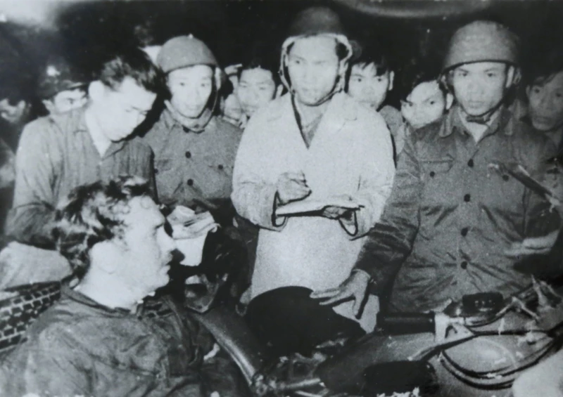 Nhà báo Phạm Thanh (người mặc áo khoác trắng) cùng nhà báo Đỗ Quảng (người đầu tiên, bên trái), phỏng vấn phi công lái máy bay B52 Mỹ bị bắt tại bãi đá Phương Liệt, Hà Nội đêm 25/12/1972. Ảnh: Bảo tàng Báo chí Việt Nam