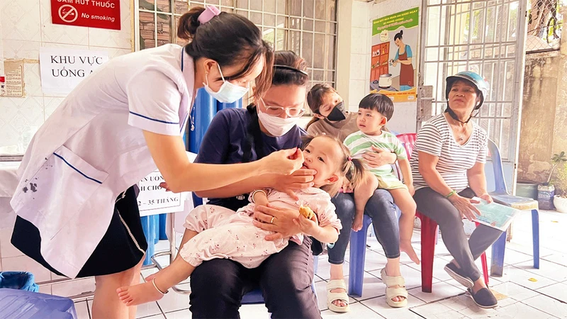 Cộng tác viên sức khỏe cộng đồng cho trẻ uống Vitamin A tại Trạm Y tế Phường 1, Quận 4, Thành phố Hồ Chí Minh.