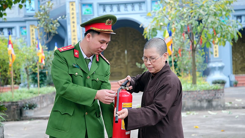 Cán bộ Công an xã Yên Mỹ, huyện Thanh Trì, Hà Nội hướng dẫn ni sư chùa Thanh Lan sử dụng bình cứu hỏa. Ảnh: HUY HOÀNG
