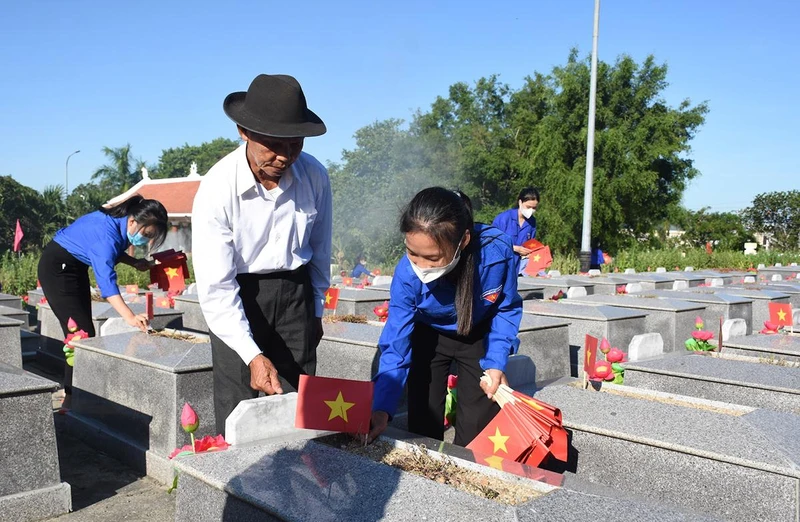 Ông Nguyễn Bá Sanh hướng dẫn các em đoàn viên thanh niên của xã Hòa Phong cắm cờ Tổ quốc lên phần mộ từng liệt sĩ.