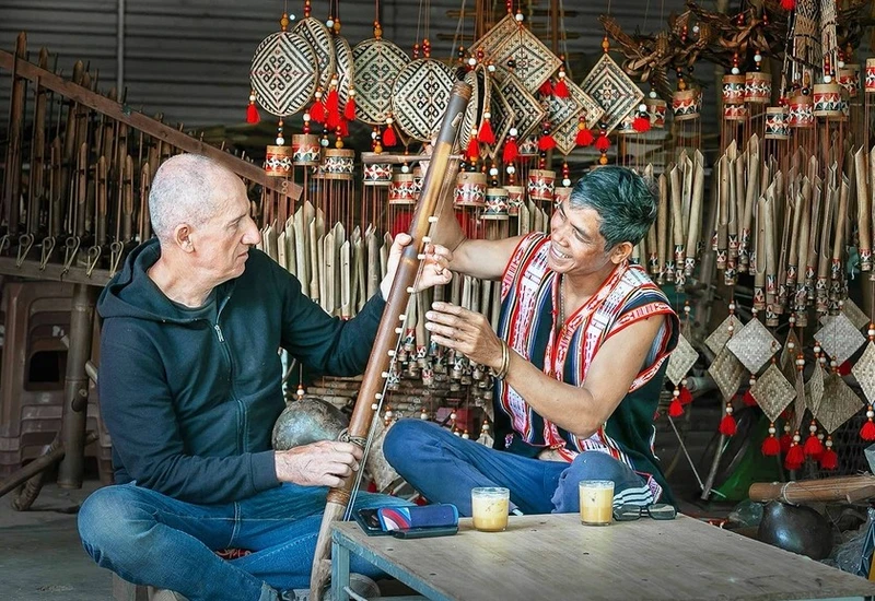 Du khách người Ý thích thú tìm hiểu các nhạc cụ truyền thống Gia Rai dưới sự hướng dẫn của Nghệ nhân Ưu tú Rơ Châm Tih. Ảnh: Nguyễn Linh Vinh Quốc
