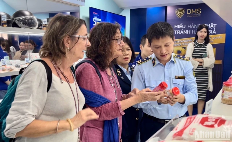 Cán bộ Tổng cục Quản lý thị trường hướng dẫn khách du lịch người nước ngoài phân biệt các sản phẩm thật-giả.