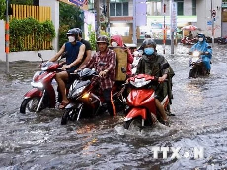 Người dân vất vả di chuyển trên đoạn ngập sâu ở đường Quốc Hương (thành phố Thủ Đức). (Ảnh: Hồng Giang/TTXVN)