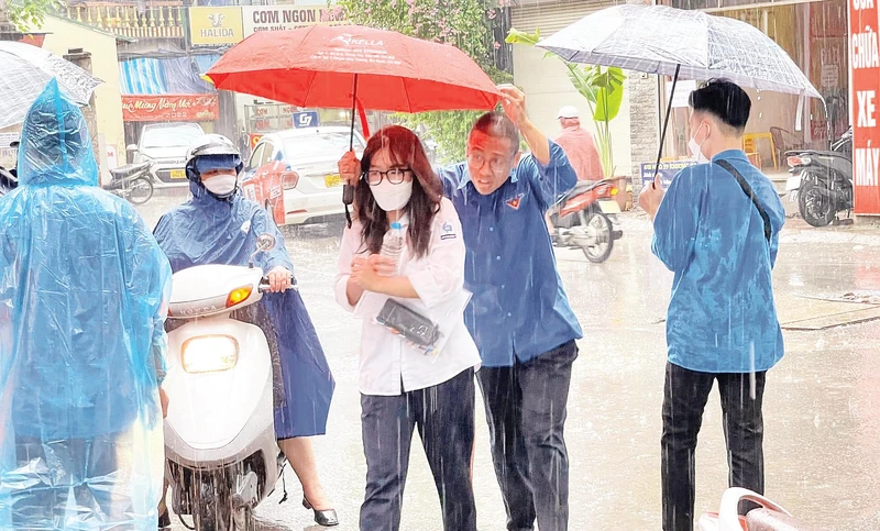Thanh niên tình nguyện che ô, hỗ trợ thí sinh vào phòng thi.