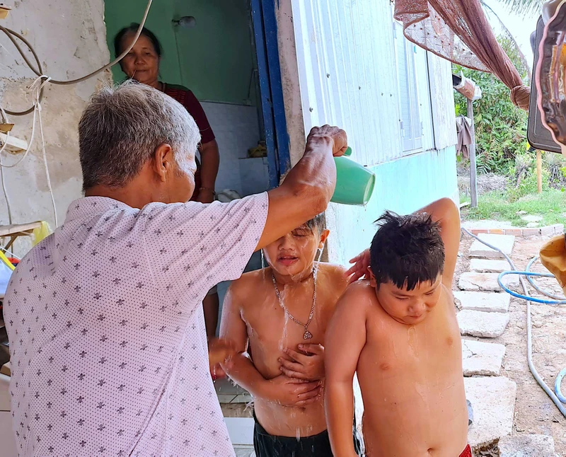Bé Tuấn Khải, Tuấn Quy (ấp Minh Hà B) được người nhà dội rửa lại bằng ít nước ngọt sau khi tắm nước mặn dưới vuông tôm.