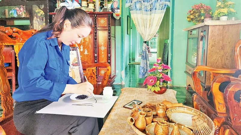 Chị Phượng tỉ mỉ gắp từng hạt gạo vào khung hình đã phác thảo.