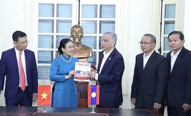 Bà Nguyễn Phương Nga tặng Chủ tịch Ủy ban Hòa bình và Đoàn kết Lào Sommad Pholsena cuốn đặc san "60 năm hữu nghị Việt Nam-Lào: Chung dãy Trường Sơn" của Tạp chí Thời Đại. (Nguồn: Báo Hà Nội mới)