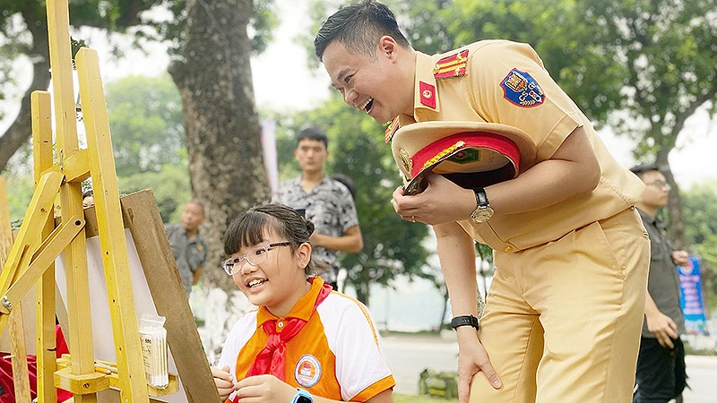 Cán bộ cảnh sát giao thông hào hứng với tác phẩm của thí sinh tại cuộc thi vẽ tranh "Thiếu nhi Thủ đô với an toàn giao thông" trong khuôn khổ Ngày hội.