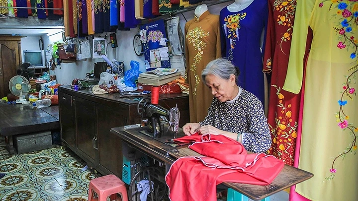 Bà Lê Thị Quyến, chủ hiệu áo dài Vinh Trạch ở phố Lương Văn Can, quận Hoàn Kiếm (Hà Nội) dù tuổi cao nhưng vẫn miệt mài bên bàn máy để trực tiếp làm ra những sản phẩm áo dài mang đúng thương hiệu Trạc