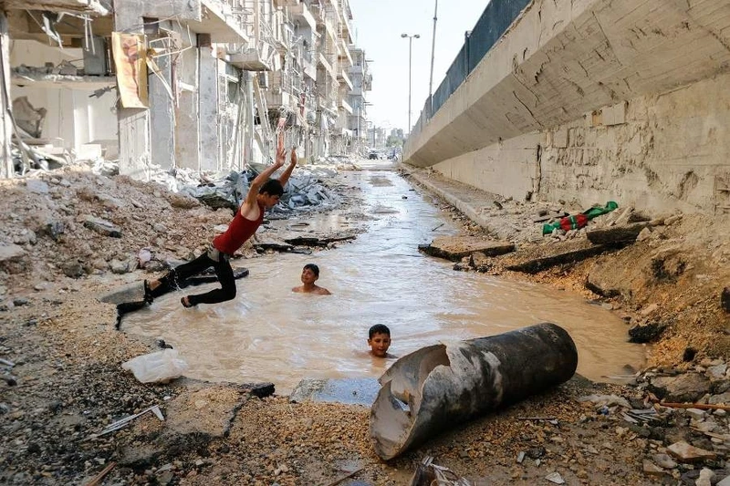 Trẻ em bơi trong một hố bom tại khu phố Al-Shaar. (Hosam Katan)