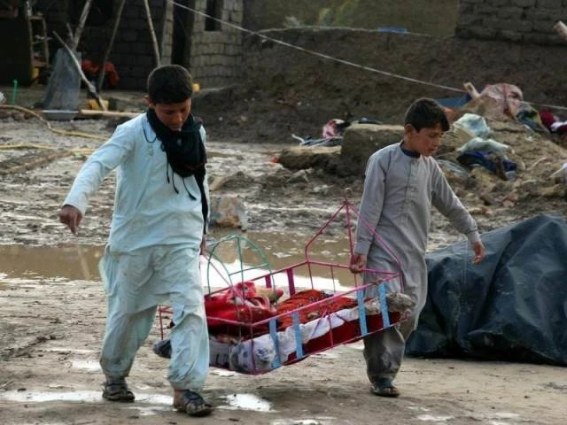 Hai bé trai tận dụng đồ đạc còn sót lại sau trận lũ quét tại Kandahar. (Ảnh: The Courier)