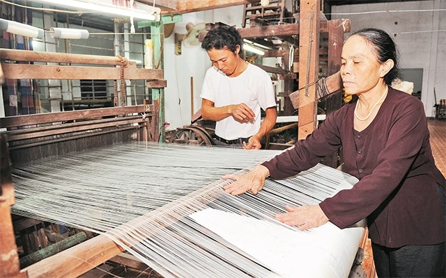 Nghệ nhân Phan Thị Thuận kiểm tra sản phẩm lụa tơ tằm. Ảnh: TRẦN HẢI