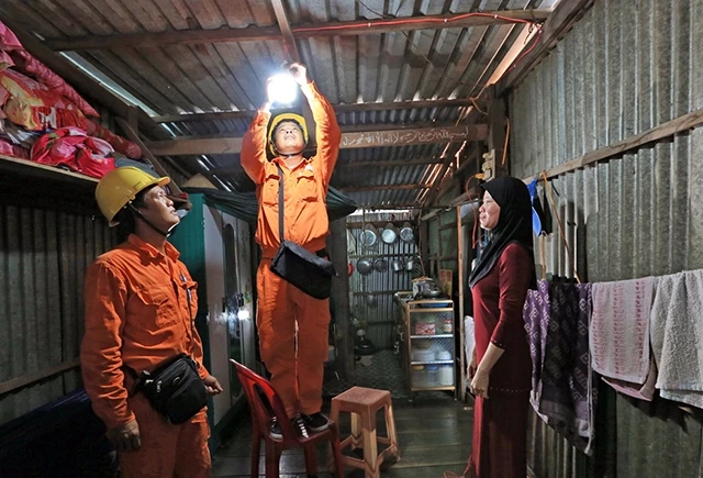 Công nhân Điện lực Châu Đốc (Công ty Điện lực An Giang) sửa chữa và lắp bóng tiết kiệm điện miễn phí cho các hộ nghèo đồng bào dân tộc thiểu số trên địa bàn huyện Châu Đốc. Ảnh: NGỌC HÀ
