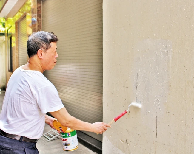 Ông Nguyễn Phi Cơ lăn sơn xóa quảng cáo trên tường nhà dân.