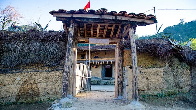 Nhà cổng truyền thống với mái ngói, cột gỗ và tường vây đắp đất.